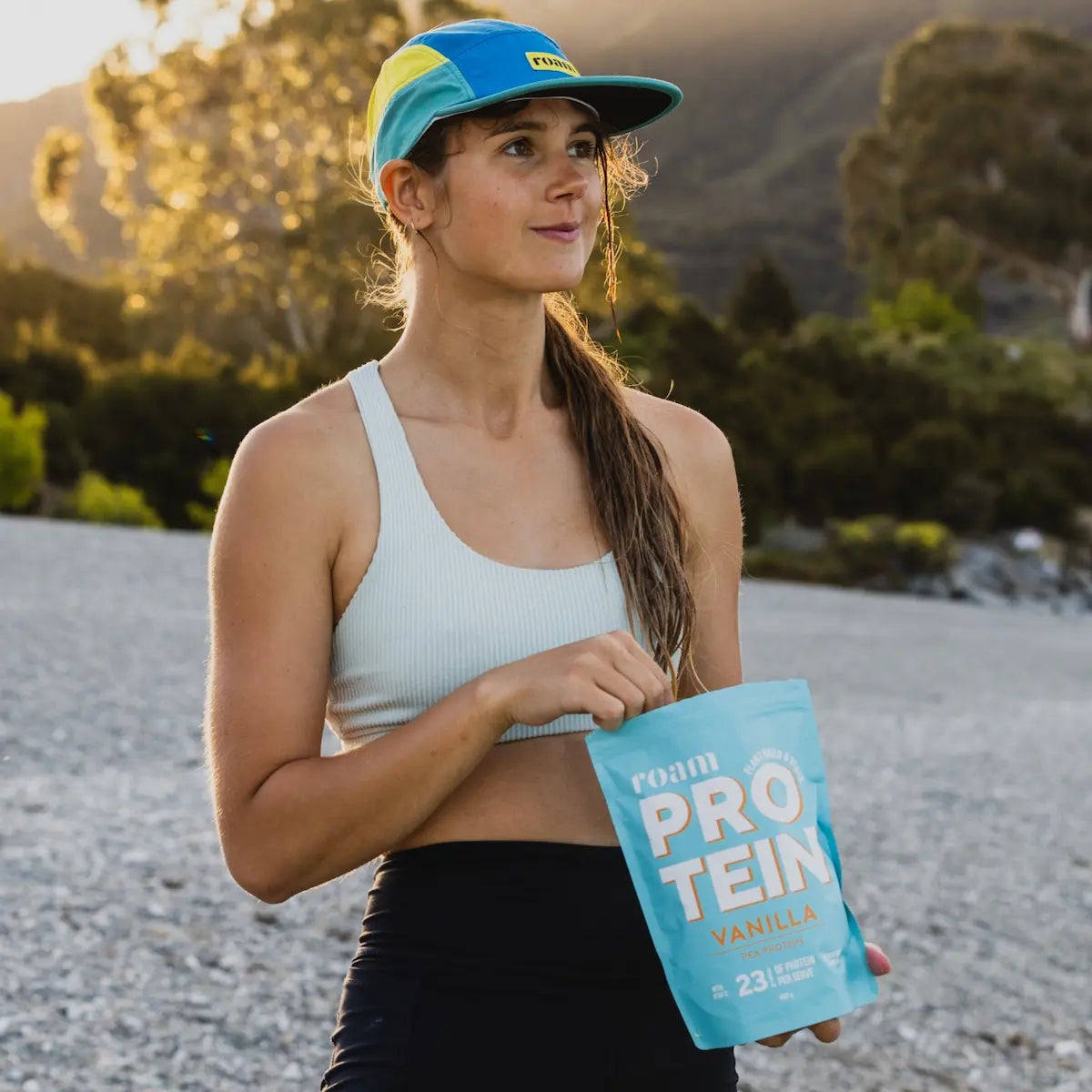 Female athlete with hat holds packet of Roam Protein outdoors