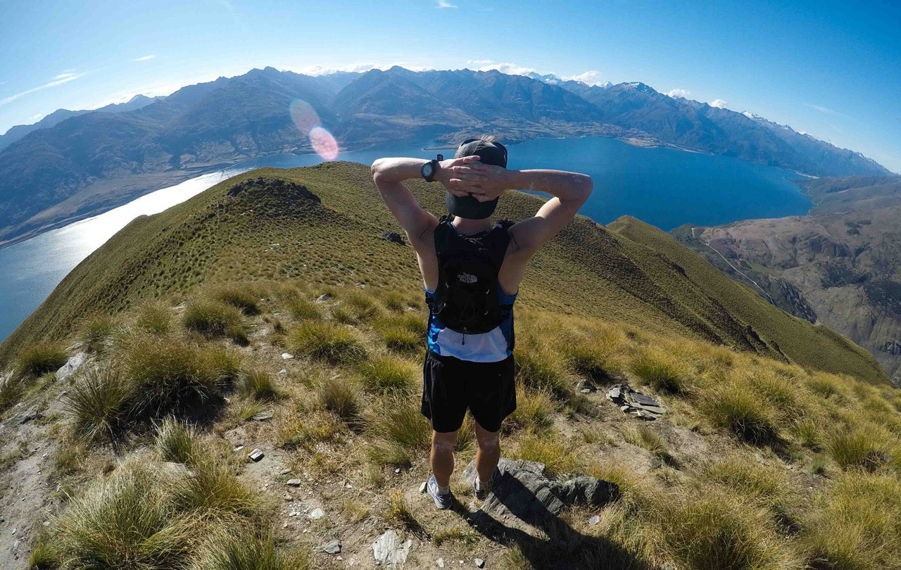 Back of Male runner looking over view of lake from top of mountain | Roam | NZ Australia