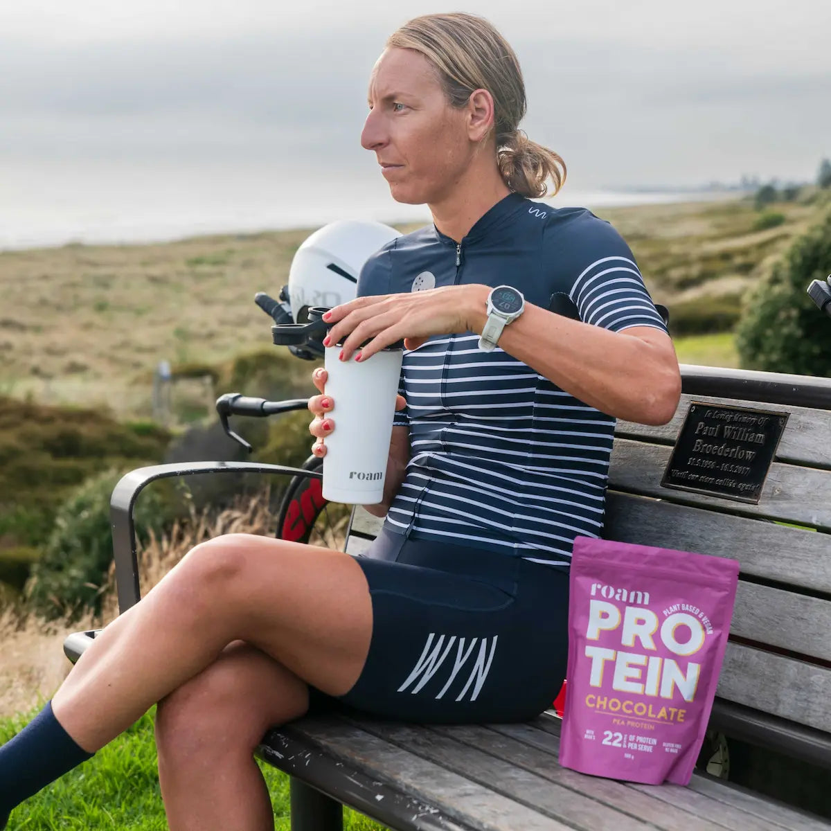 Triathlete sits on a bench and has protein shake after a bike ride