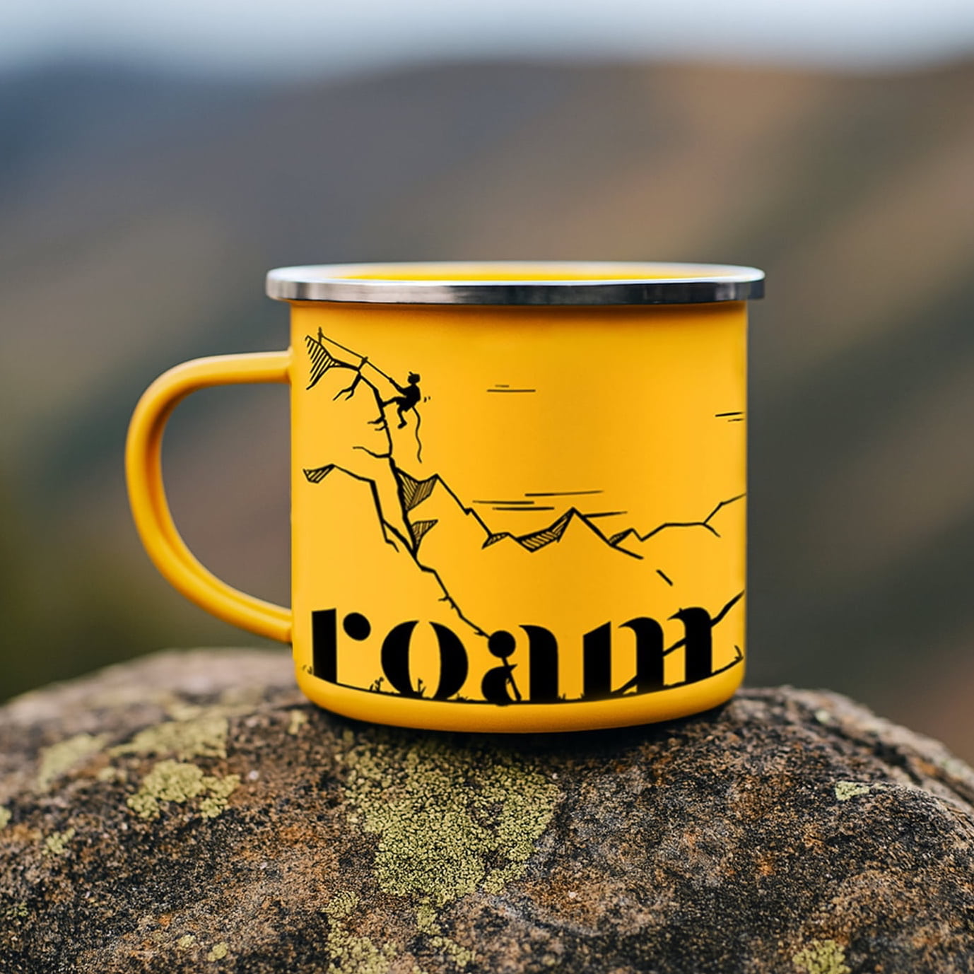 Yellow mug with mountain design and 'roam' text on a rock with blurred natural background